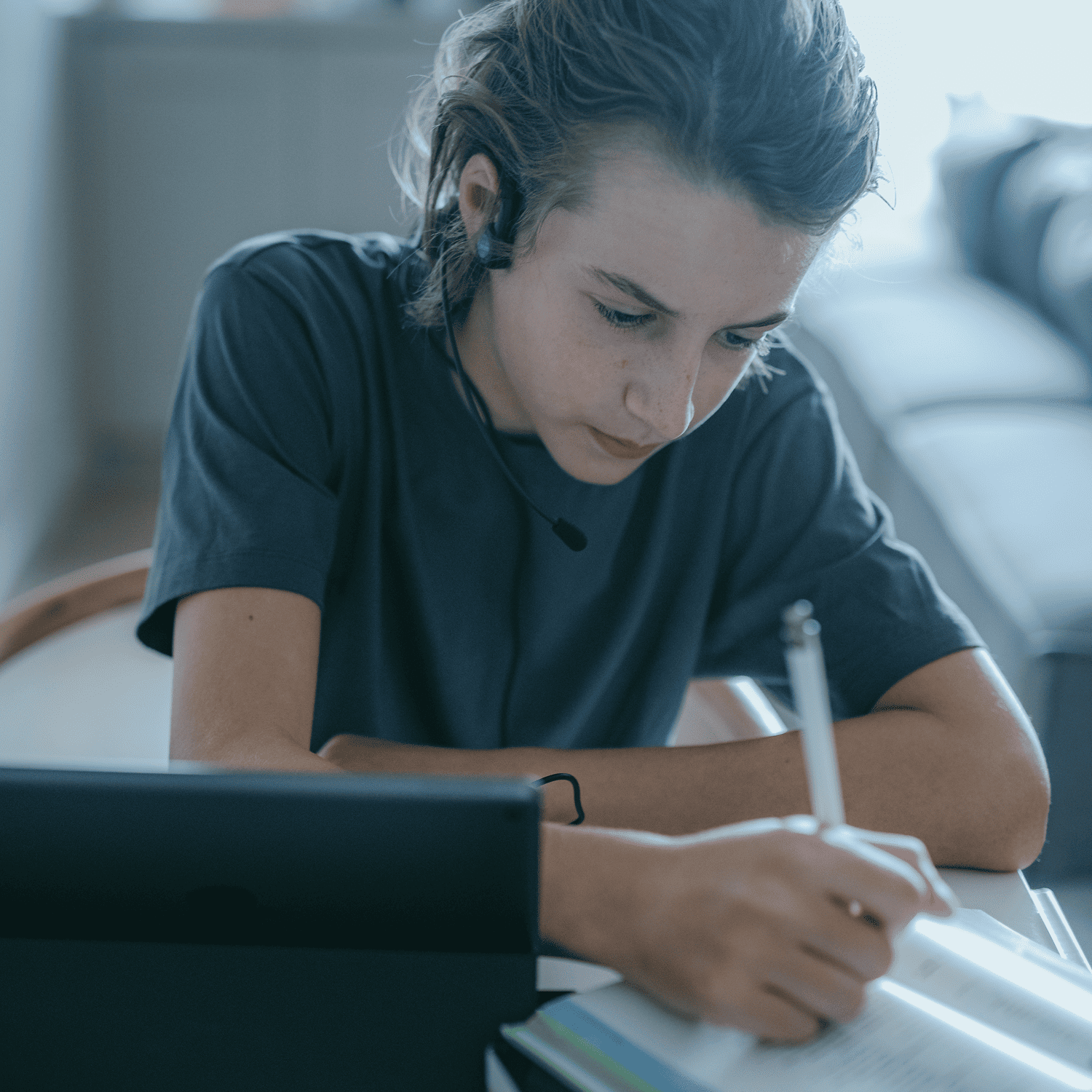 Student wearing a forbrain headset writes notes at a desk while studying with a laptop.